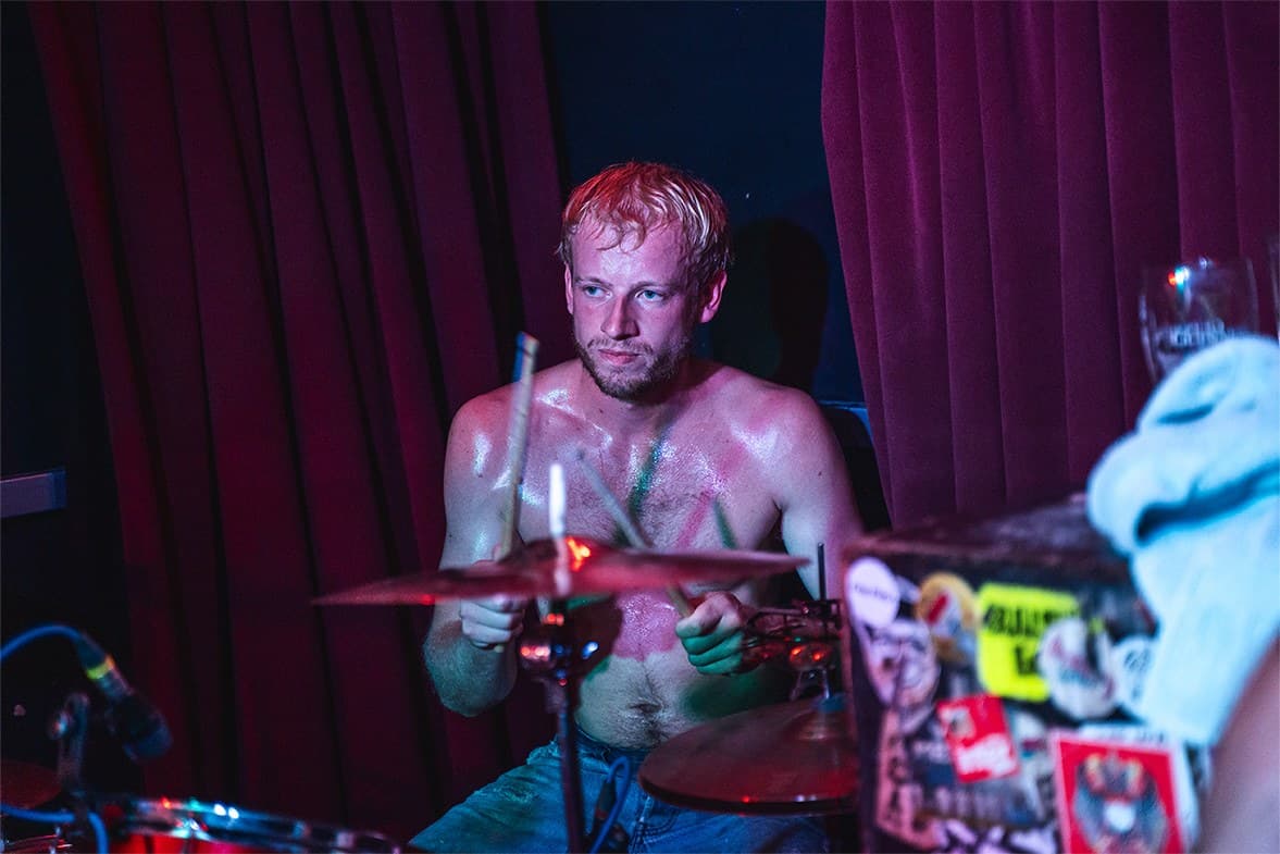 Drummer mid-set, shirtless, under red light